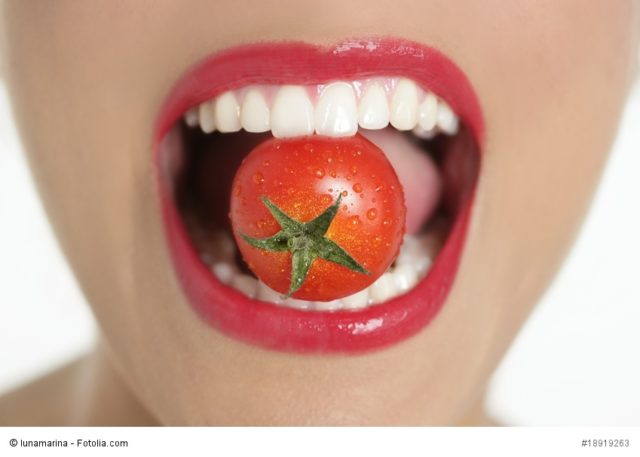 Eating a red tomato macro of woman teeth and red lips mouth