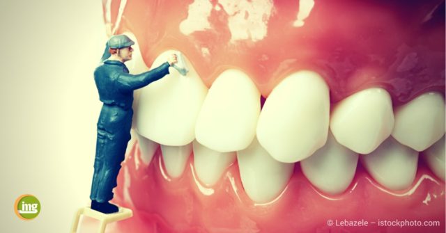 Mann auf Leiter putzt riesengroße Zahnprothese