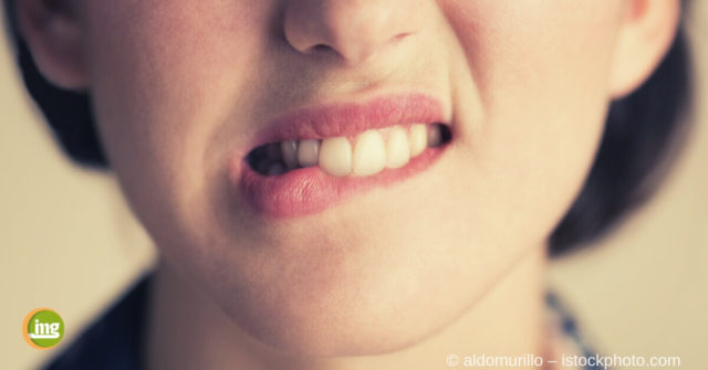 Junge Frau beißt sich auf Lippe und spürt Zahnstein an den Zähnen.